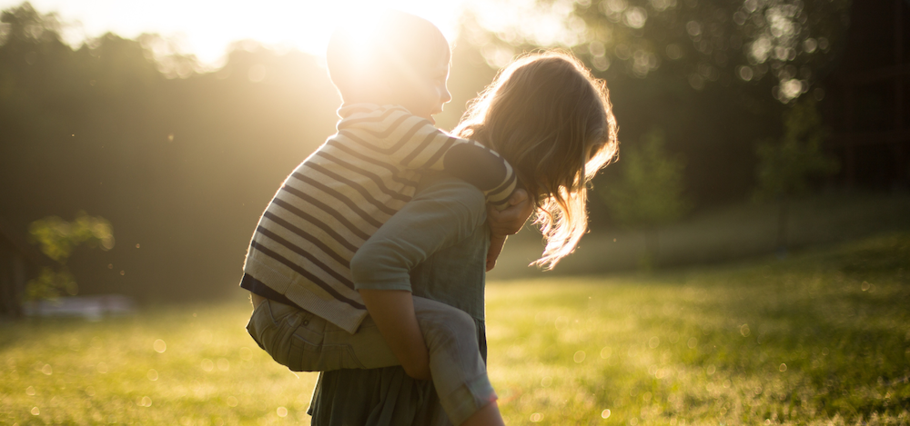 a young girl gives another child a piggy back ride
