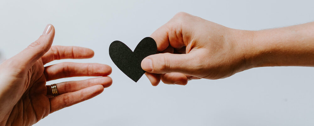 a hand holding a paper heart passes it to another hand