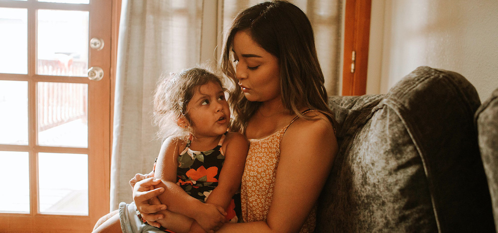 a young woman holds a child in her lap as they look at each other